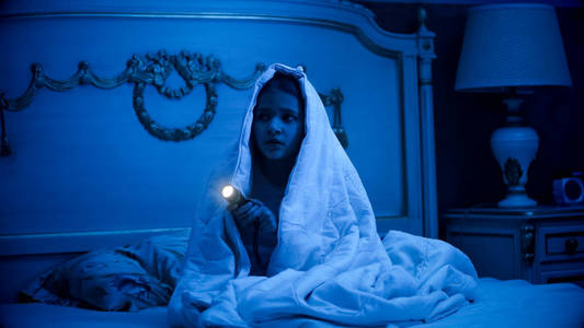 害怕的女孩坐在黑暗的卧室与 glashlight照片