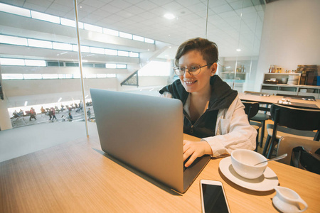 戴眼镜的妇女在笔记本电脑到机场工作。小工具互联网博客和无线技术