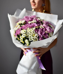 美丽的女人捧着菊花的花束, 白色和紫色快乐的微笑