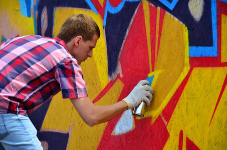 一位年轻的红头发涂鸦艺术家在墙上画了一幅新的涂鸦。在墙特写画涂鸦的过程的照片。街头艺术的概念与非法破坏