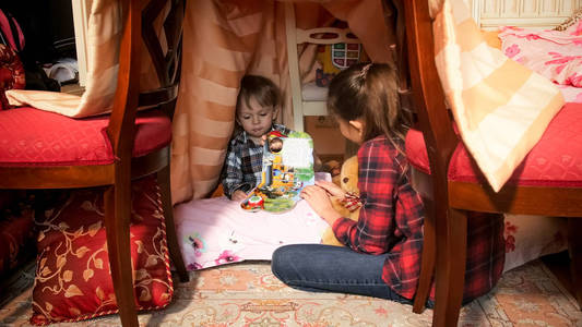 可爱的蹒跚学步的男孩在卧室的圆锥形帐篷帐篷读书