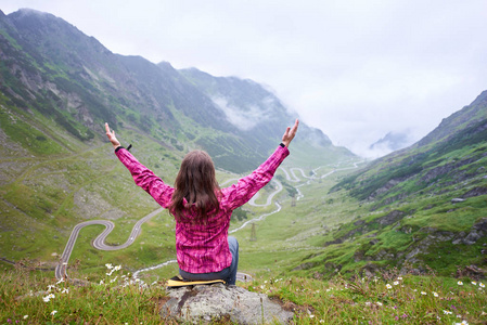 妇女游客坐在她的双臂敞开, 并期待与背景 Transfagarashan 公路, 最美丽的道路, 在欧洲, 罗马尼亚。后退视图