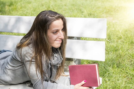 读一本书在公园的长凳上的年轻女子