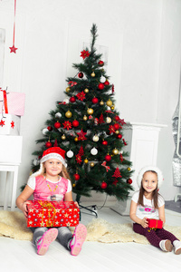 两个女孩在他们的手坐在树下的礼物的圣诞服饰