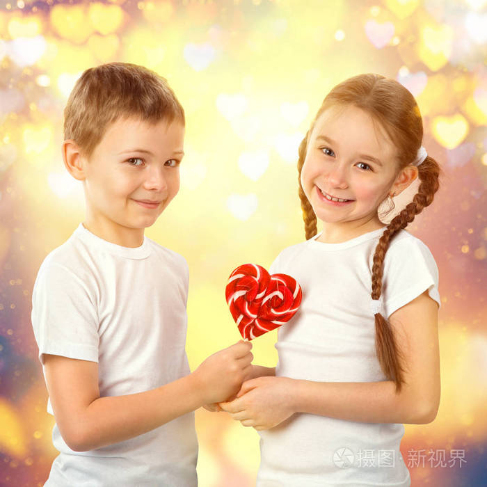 男孩给出了一个小女孩糖果红色棒棒糖在心的形状.情人节那天艺术肖像