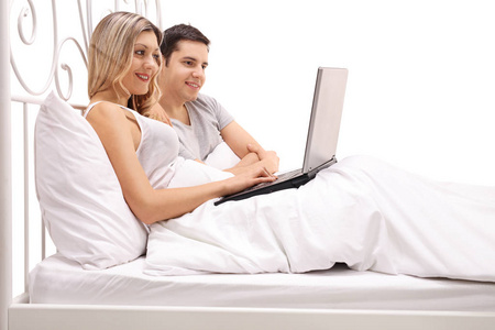 对夫妇躺在床上，看着一台笔记本电脑