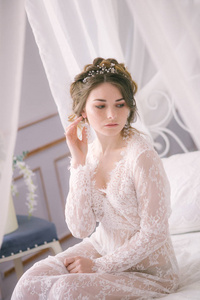 美丽的新娘肖像。新娘的早晨。婚礼的早晨。化妆。有锥形和金发的新娘。脆弱的新娘白色花边睡衣