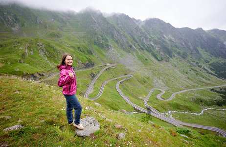 快乐的女人旅行者微笑着向相机, 竖起大拇指, 站在山前的 Transfagarasan 路 copyspace Romanie 