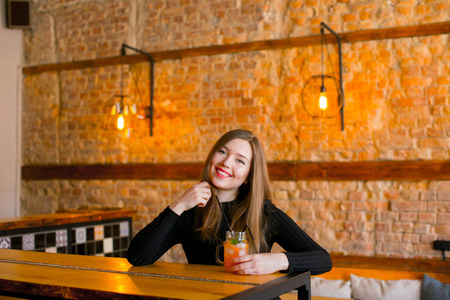 满意的女孩坐在旁边的木桌与杯柠檬水在咖啡馆和放松