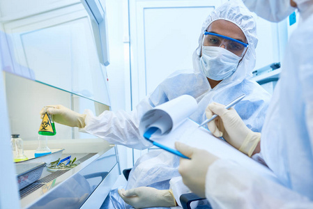 两名科学家在医学研究实验室中佩戴防护服和口罩的画像照片