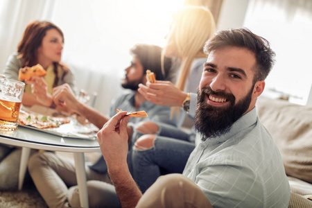 微笑的朋友在家里吃比萨饼和喝啤酒。休闲人食物和幸福概念