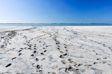 白色的盐滩的治疗泥。脚步声跟踪到湖边。白色的沙滩和美妙的蓝天