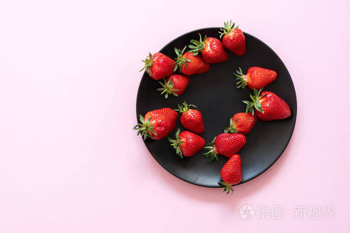 在黑色的盘子上的新鲜草莓反对粉红色粉彩针的背景。复制空间。从上面查看