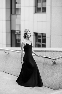 漂亮的女人在长晚上黑色礼服摆在花岗岩楼梯台阶上