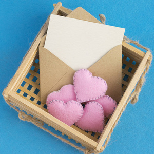 空邀请卡。老信封在木柳条篮子与长毛绒粉红色的心脏在蓝色背景