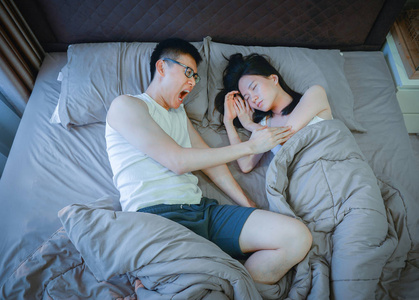 愤怒的亚洲夫妇晚上在床上打架照片