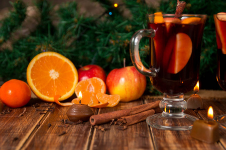 木制的桌子上香料和水果的甜酒。圣诞装饰品在背景中。冬季气候变暖饮品周围的配方成分