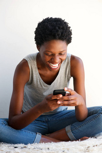 在家里微笑和使用手机的欢快的年轻非洲裔美国妇女的肖像