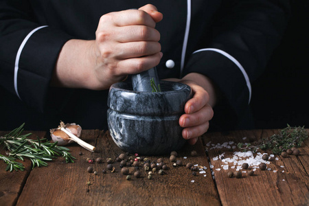 女厨师在黑色背景下用砂浆敲打香料和香草