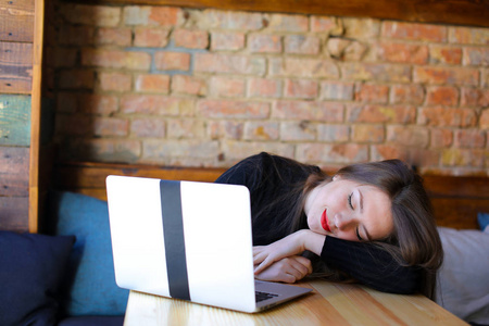 疲倦的学生睡觉和坐在现代笔记本电脑附近在咖啡馆在沙发上