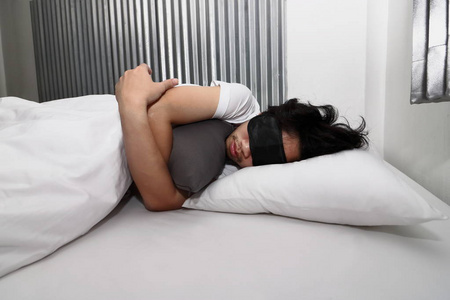 戴面具的年轻亚裔男子舒适地睡在家里的床上