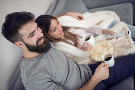 快乐的年轻夫妇坐在沙发上的家与爆米花和看电视