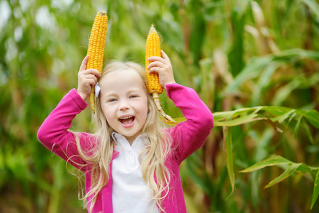 可爱的女孩笑捧玉米棒子照片
