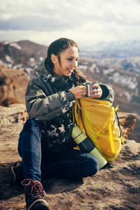 坐在悬崖边上的快乐的年轻女孩, 喝热茶和享受自然
