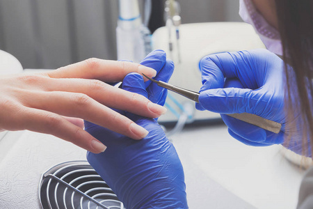 特写镜头的指甲在蓝色橡胶手套和医疗面罩删除指甲上的女性指甲使用的工具。美容院的专业修指甲与指甲护理程序