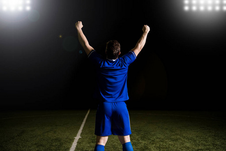 年轻橄榄球运动员的后方看法在蓝色制服站立用手胳膊在赢取比赛以后上升了