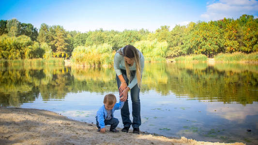 可爱的蹒跚学步的男孩与年轻母亲在湖附近公园