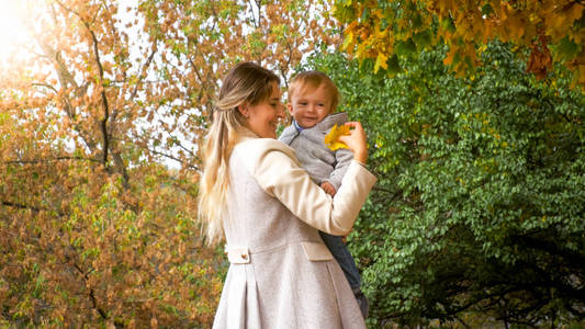 在公园里看黄色叶子的孩子快乐微笑的母亲的画像