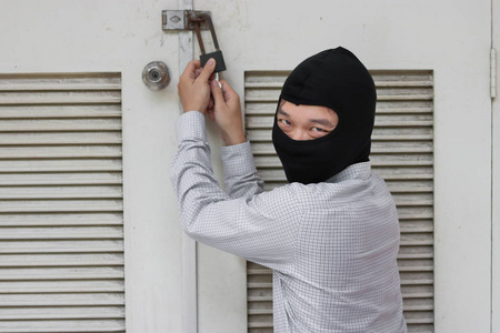 蒙面强盗使用锁领工具闯入和进入房子。犯罪概念