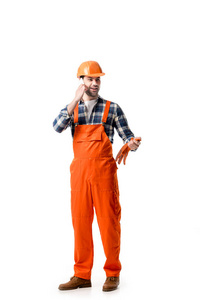 年轻的修理工在橙色整体和硬帽子谈论在电话上孤立的白色