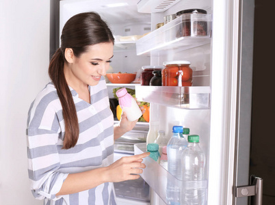 家附近开冰箱的年轻妇女与瓶酸奶