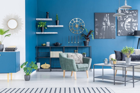 现代起居室蓝色墙上的黑色画绿色扶手椅和植物
