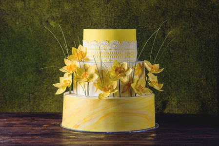 美丽的家黄色婚礼三层蛋糕装饰着红色的春天的花朵。甜点的概念花卉趋势