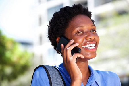 美丽的年轻黑人妇女的肖像在户外和微笑谈论智能手机