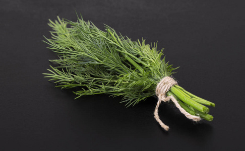 在黑色背景上绑着绳子的一束新鲜的莳萝照片