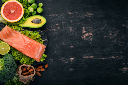 健康食品。鱼鲑, 鳄梨, 花椰菜, 新鲜蔬菜, 坚果和水果。在黑色的背景。顶部视图。复制空间