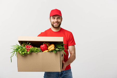 送货理念 英俊的白种人杂货送货员身着红色制服, 配有新鲜水果和蔬菜的杂货箱。