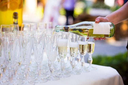 侍者倒进一杯香槟。在白色桌子上，一排空的香槟杯的空杯子。Furshet，餐饮。眼镜的香槟或红酒