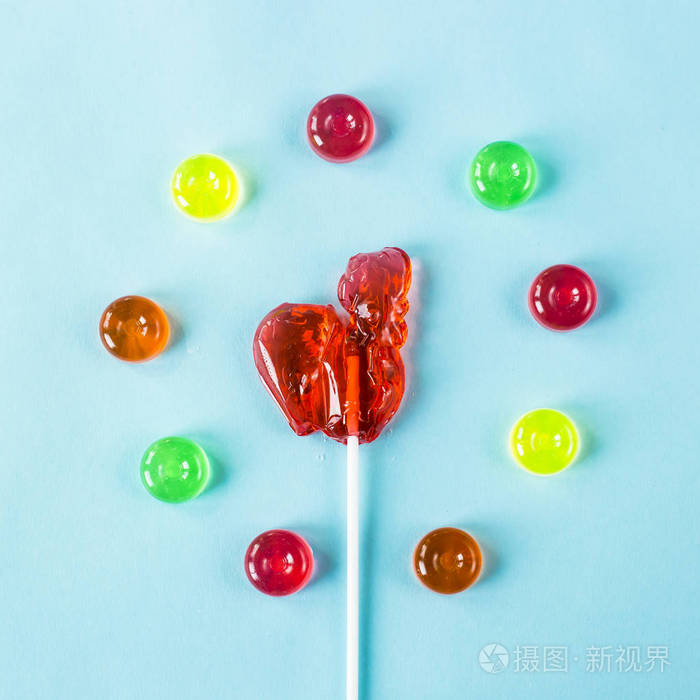 红棒糖的形式公鸡在一杯五颜六色的糖果复古糖果在蓝色背景上顶部视图