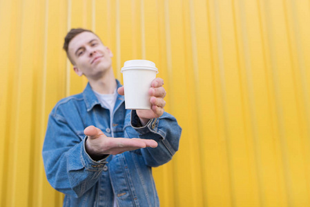 一个年轻人站在一堵黄色的墙的背景上, 并给他一杯咖啡。聚焦和特写杯