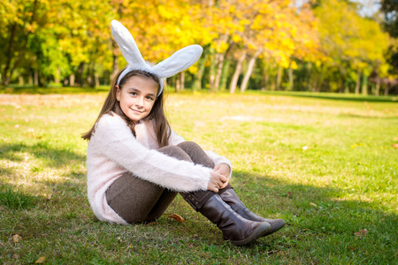 在户外在美丽的秋日与兔子耳朵在她头上的可爱小女孩