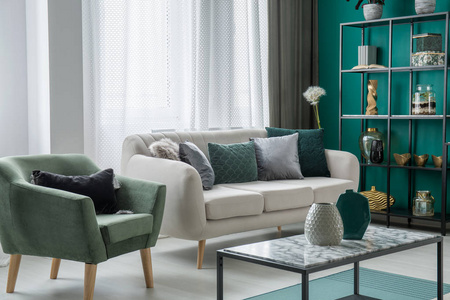 绿色和银色的装饰枕头放在一个浅灰色的沙发上, 站在客厅内的窗户, 扶手椅和大理石桌子