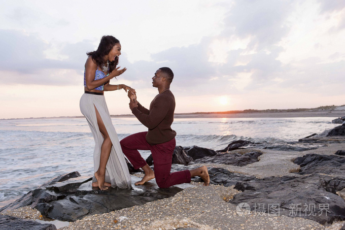 中年男子跪在海边的岩石上向年轻女子求婚