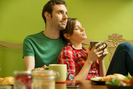 女人喝咖啡年轻夫妇吃早饭时候女人用智能手机年轻夫妇吃早饭,男人倒