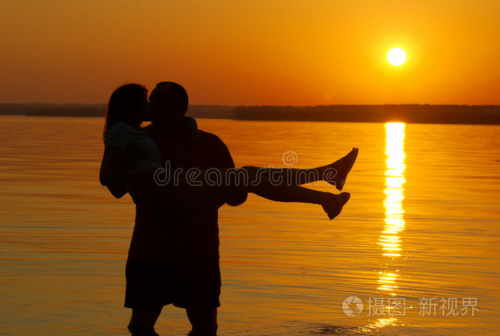 恩爱的年轻夫妇夕阳下亲吻的情侣剪影海滩上的情侣年轻情侣拥抱微笑