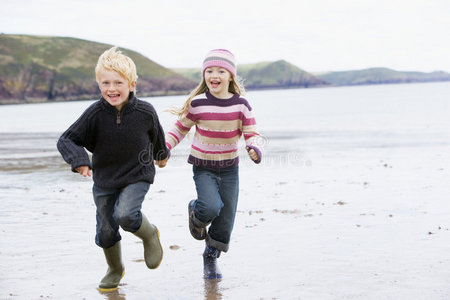 两个小孩手牵着手在沙滩上奔跑